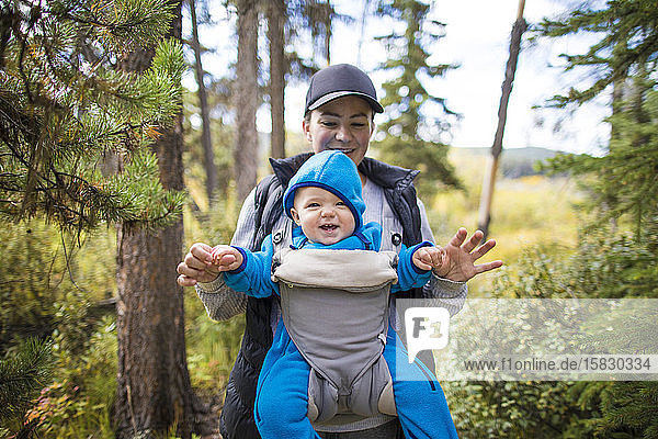 Mother laughing with her baby during walk through forest.