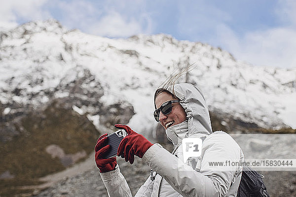 Wanderin mit benutzter Handykamera an windigem Tag in den Bergen.