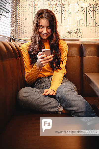 Glückliche Teenagerin benutzt Smartphone  während sie im Café sitzt