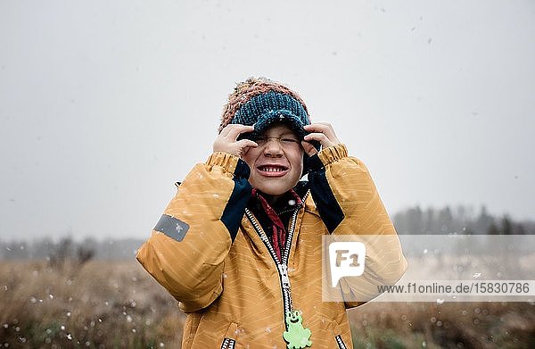 boy covering his face with his hat whilst playing in the snow