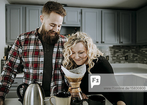 junge Frau riecht Morgenkaffee  während Ehemann mit Bart zuschaut