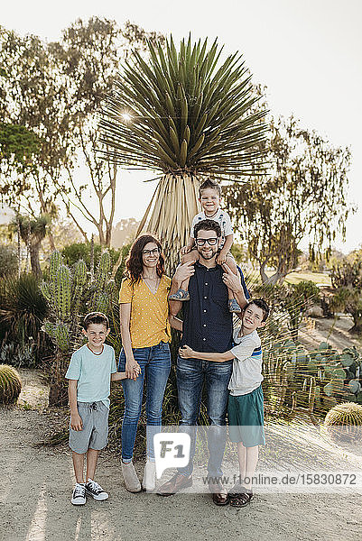 Porträt einer Familie  die im sonnigen Kaktusgarten vor der Kamera lächelt