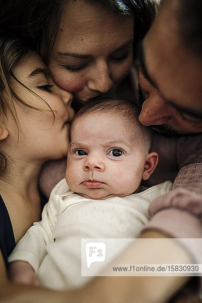 Papa, Mama und große Schwester küssen Neugeborene