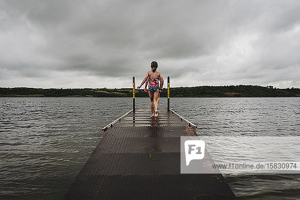 Little Girls Walk on Dock Toward Water on a Cloudy Day at the Lake