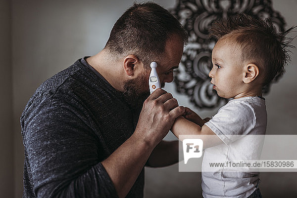 One year old boy taking fatherâ€™s temperature at home during isolation
