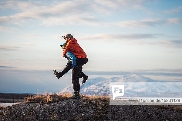 Woman giving man piggyback with mountains behind them