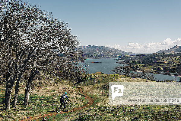 Eine junge Frau fährt mit dem Fahrrad einen Weg entlang  der den Columbia River überblickt.