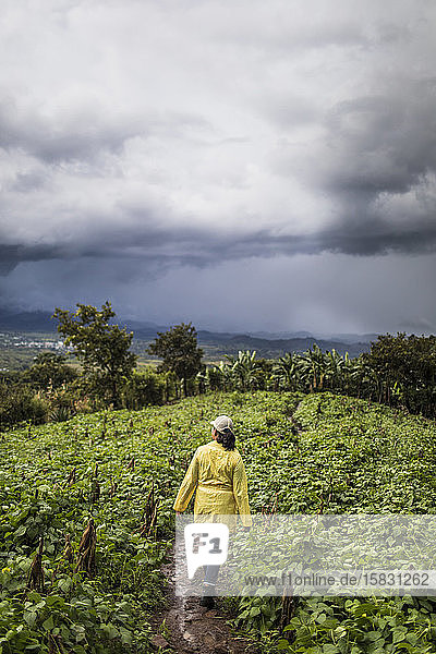 Junge Frau in gelbem Mantel geht durch üppiges Feld in Guatemala.