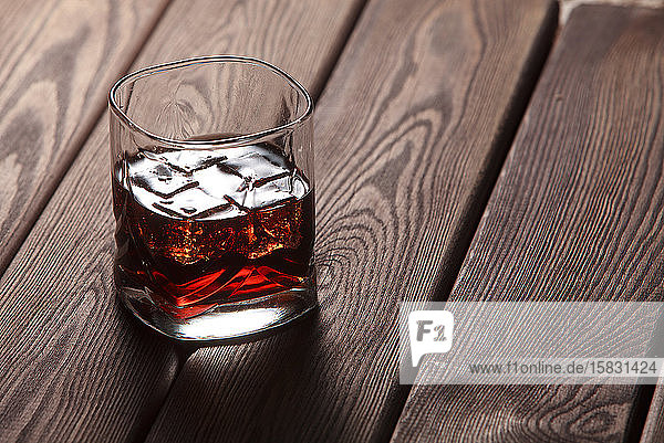 Whisky im Glas mit Eis auf dunklem Holzgrund