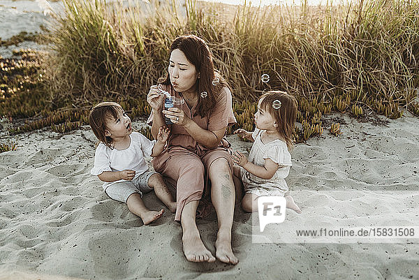 Mutter mit jungen Zwillingstöchtern  die am Strand Seifenblasen blasen