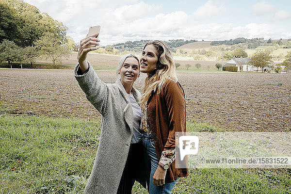 Two female friends taking a selfie in a French countryside landscape