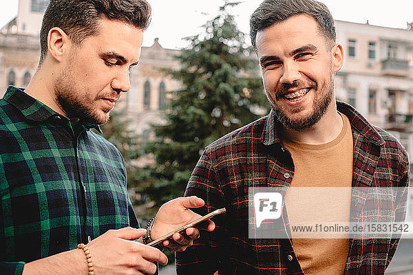 Mann benutzt Smartphone  während sein Bruder lachend neben ihm steht