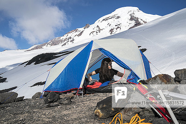 Eine Frau greift nach etwas  während sie in ihrem Zelt im Basislager  Mt. Baker  sitzt