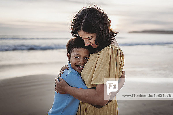 Porträt einer schönen Mutter  die ihren kleinen Sohn bei Sonnenuntergang am Strand umarmt