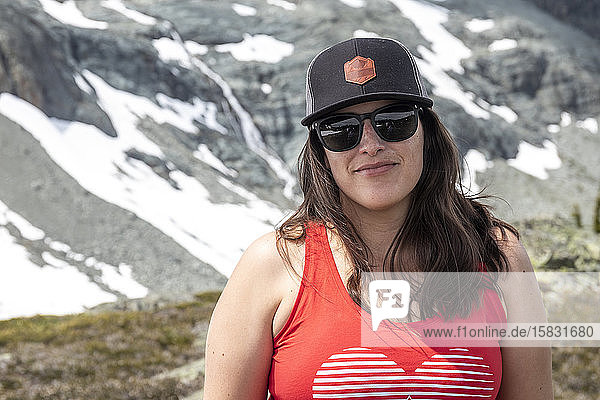 A women hiking in the mountain takes a break and smiles for the camera on a summer day in the mountains of British Columbia.