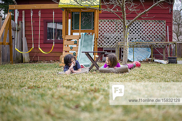 Two happy children lay on mats in their yard chatting together