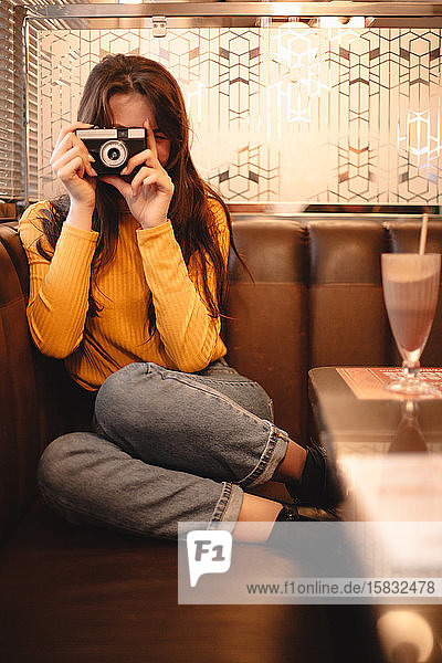 Teenager-Mädchen fotografiert mit Vintage-Kamera  während sie im Café sitzt