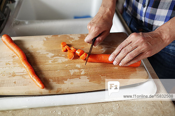 Nahaufnahme der Hände einer Frau  die eine Karotte auf einem Schneideblock schneidet
