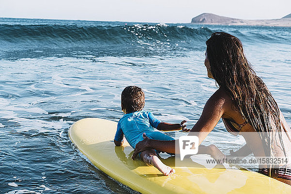 Junge Mutter und Sohn paddeln auf einem Surfbrett auf See