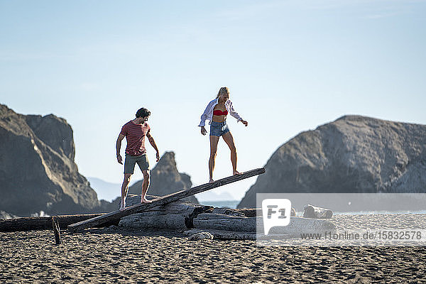 Teenager-Paar balanciert auf Treibholz-Wippe am Strand