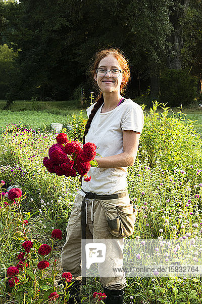 Junge lächelnde Frau hält frisch geschnittene rote Blumen im Garten