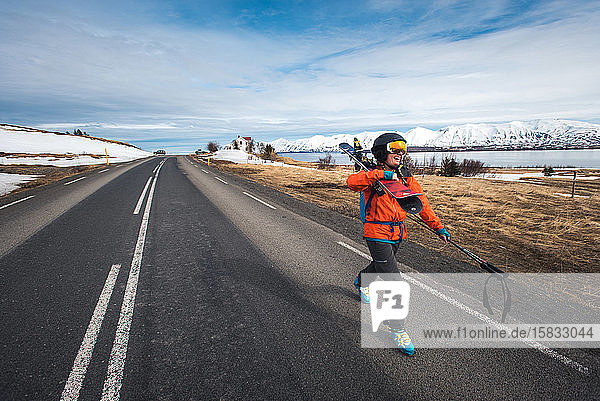 Eine Frau  die mit Skiern auf einer gepflasterten Straße in Island unterwegs ist