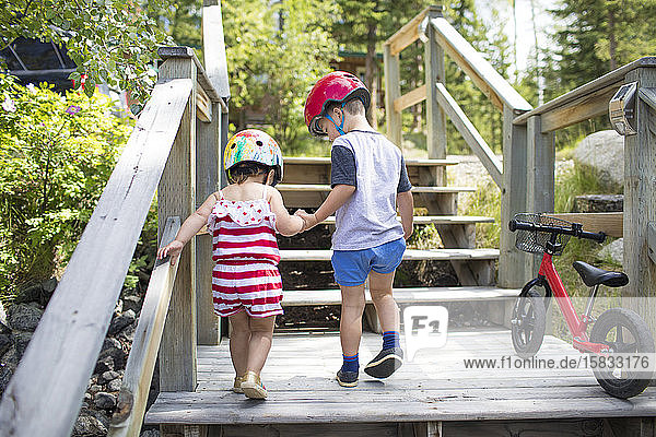 Brother holding hands with sister helping her up wooden staircase.