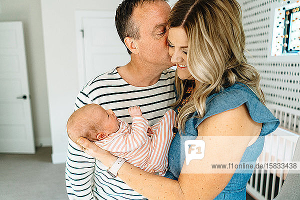 Ein Ehemann  der seine Frau auf die Wange küsst  während er ein Baby hält