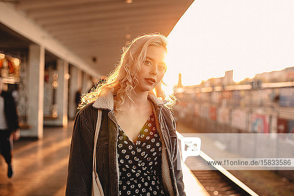 Young woman waiting for train at subway station at sunset