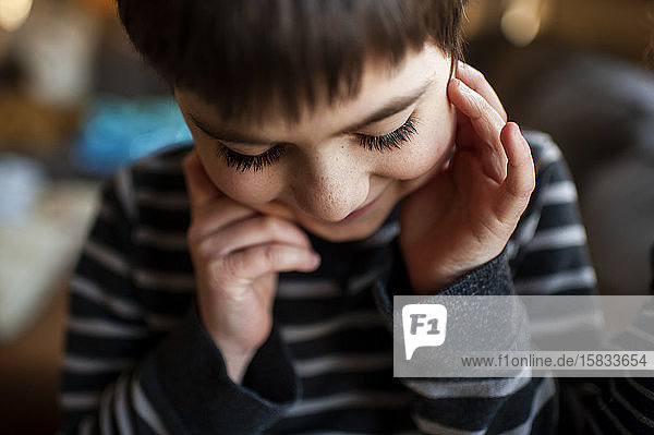 Boy 7-8 years old with long eyelashes looking down with hands by face