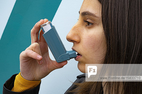 Frau  die einen blauen Asthma-Inhalator auf blauem Hintergrund inhaliert.