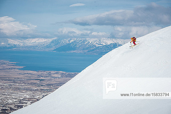 Ein Mann springt von einer Skisprungschanze auf einem Berg in Island mit Wasser im Rücken
