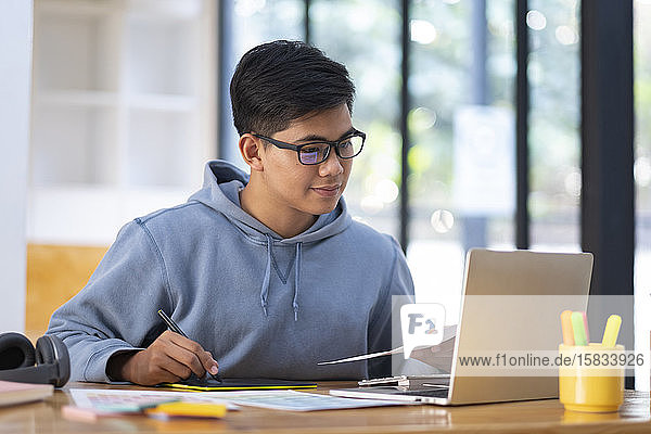 Junge Collagestudentin mit Computer und Mobilgerät beim Online-Lernen