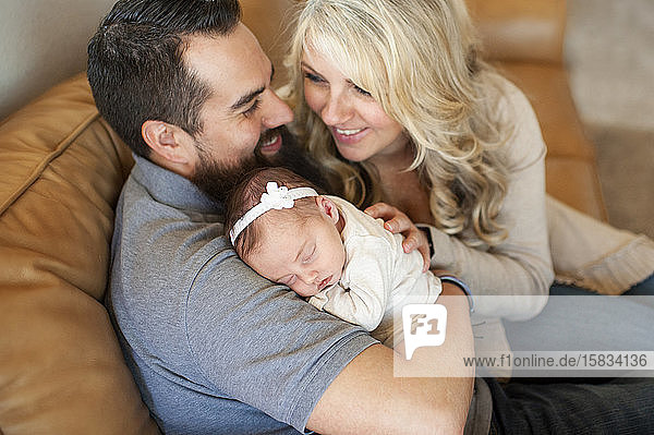 Happy smiling family holding newborn baby girl at home on couch