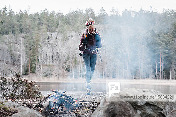 Frau  die auf einem Felsen zu einem Lagerfeuer an einem See in Schweden geht