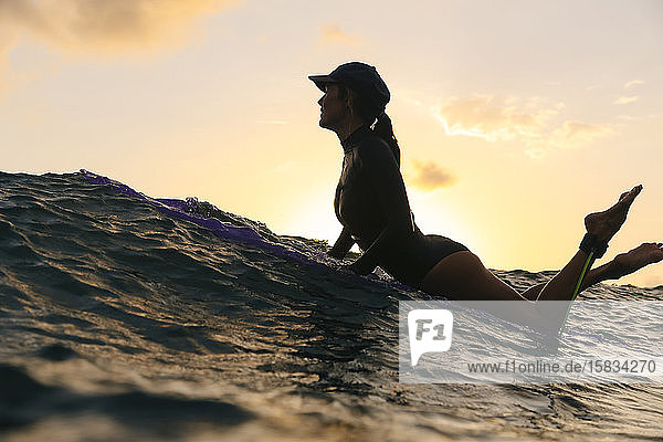 Weibliche Surferin liegt abends auf dem Surfbrett