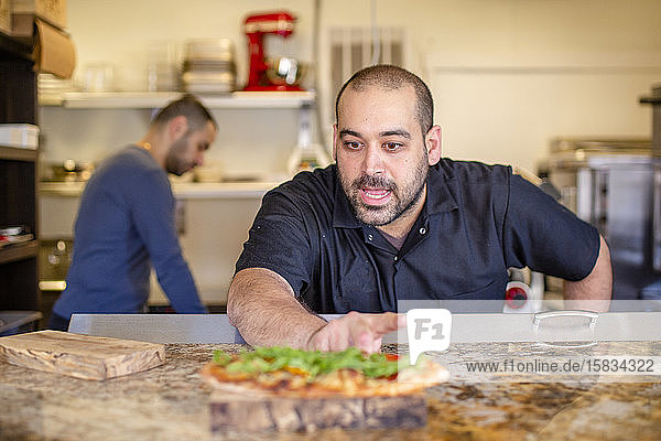 A chef leans over a kitchen counter describing a prepared dish of food
