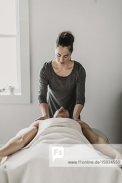 weibliche Massagetherapeutin behandelt männlichen Patienten auf Massagetisch