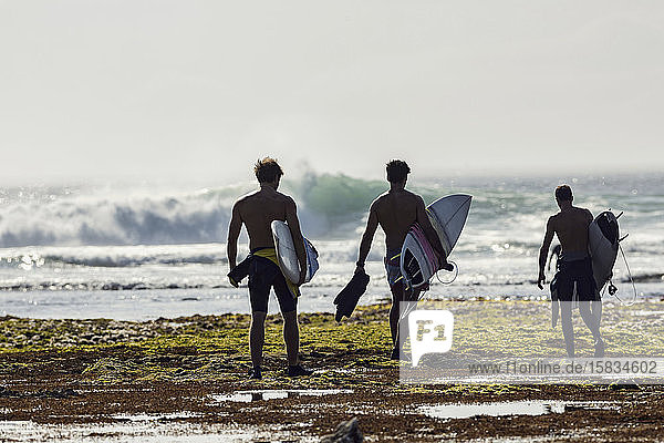 Gruppe von Männern mit Surfbrett am Strand spazieren