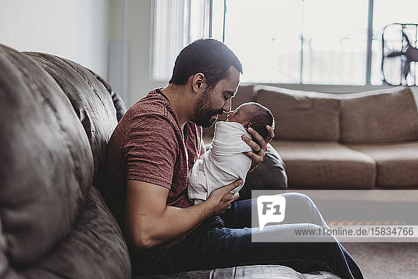 Bearded father bonding with newborn baby wrapped in white blanket
