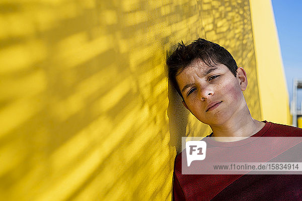 Porträt eines fröhlichen Teenagers  der vor der Kamera an einer gelben Wand lehnt