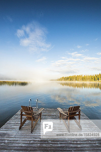 Wooden chairs on dock looking over lake at dawn