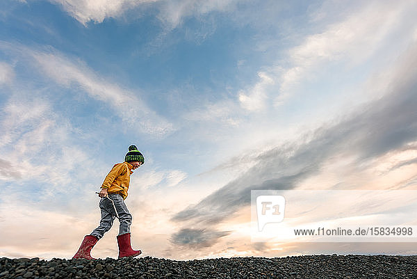 Junges Kind mit Stock am Strand im Winter in der Dämmerung