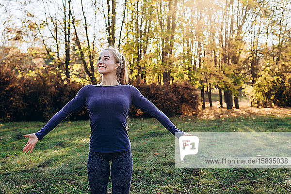 Beautiful smiling girl at morning gym in the park  looking away with arms extended.