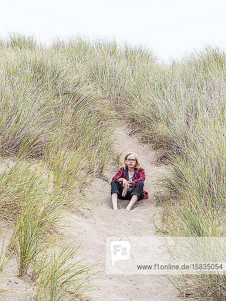 Tween boy sitting on sand trail in tall beach grass