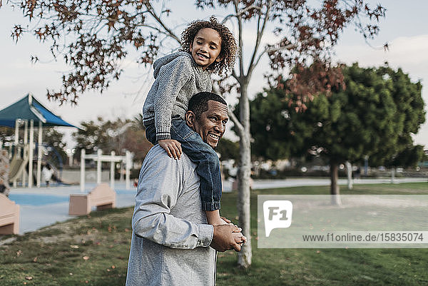 Cute boy sitting on happy father's shoulders at park playground