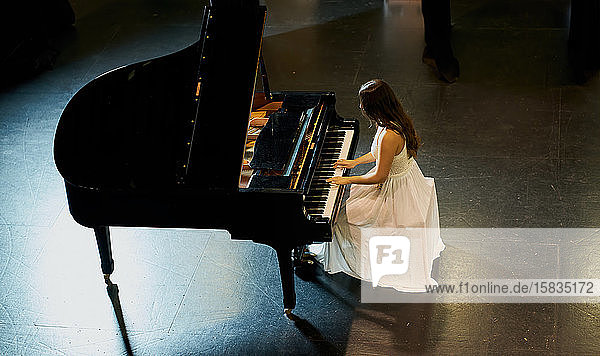 Eine Frau mit braunem Haar in einem weißen Kleid  die auf einem schwarzen Flügel mit erhobenem Deckel spielt. Blick von oben auf den Pianisten