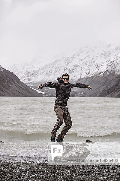 Mann im Mantel springt im Nebel vom Felsen neben dem Gletschersee.