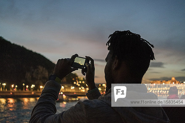 Afrikanischer Mann fotografiert nachts in Budapest von einem Boot aus