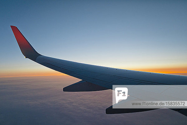 Flügel eines Flugzeugs in der Mitte der Luft bei Sonnenuntergang  das über den Planeten Erde fliegt.